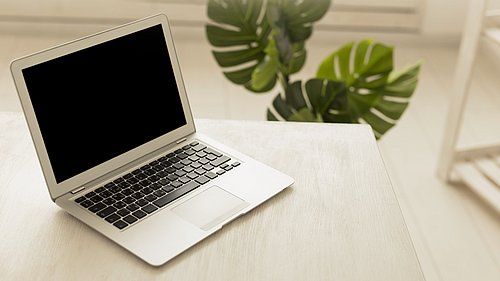 Aufgeklapptes Laptop auf Tischplatte, schwarzer Bildschirm